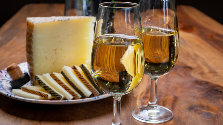 two wine glasses with a hunk of cheese and sliced cheese