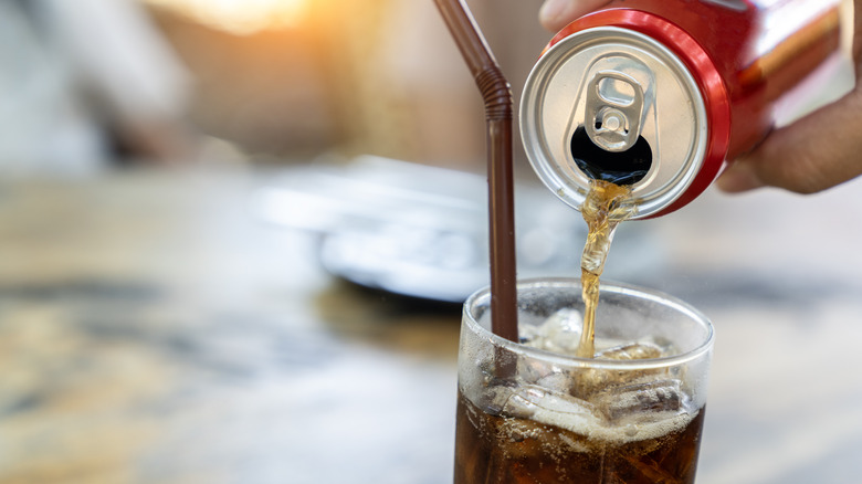 Cola being poured into a glass with a straw from a red can