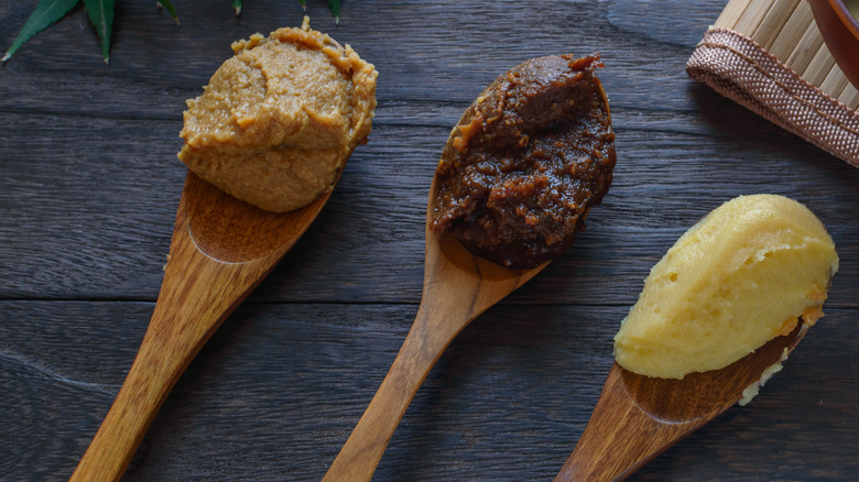 three types of miso paste in wooden spoons on a rustic Japanese background