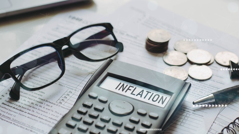 calculator with the word inflation on the screen surrounded by eyeglasses and coins