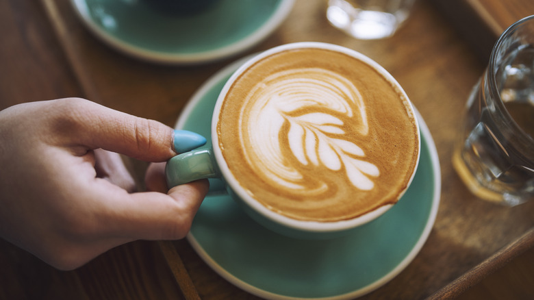 hand holding a latte topped with leaf art