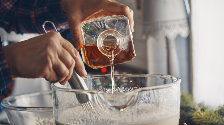 Pouring a decanter of dark liquor into a mixing bowl of homemade eggnog, and whisking them together