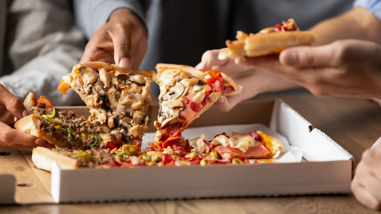 People grabbing slices of pizza from box