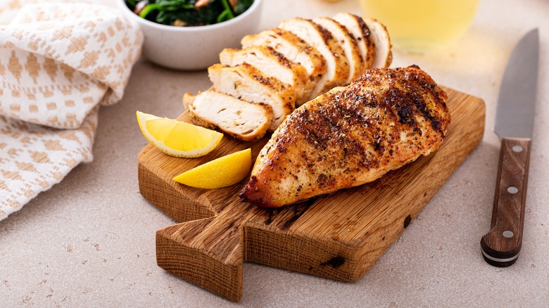 Sliced and unsliced chicken breast next to lemon on cutting board