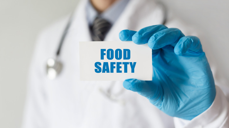 Doctor holding up 'food safety' card with blue latex gloves