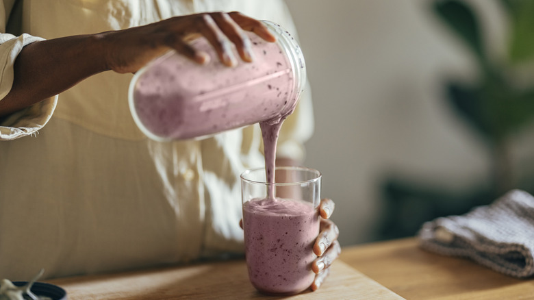 Hands pouring a smoothie into a glass