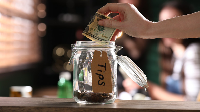 hand putting money into tip jar