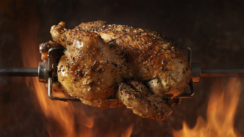 rotisserie chicken on a spit, surrounded by flames