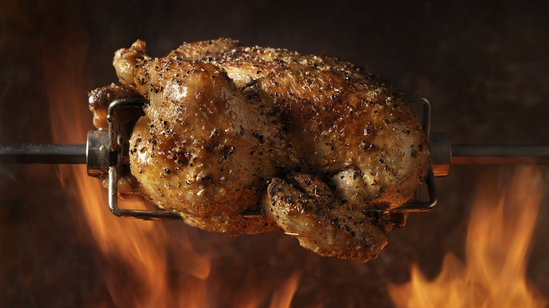 rotisserie chicken on a spit, surrounded by flames