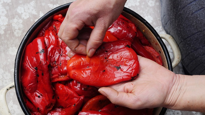 hands peeling grilled red peppers