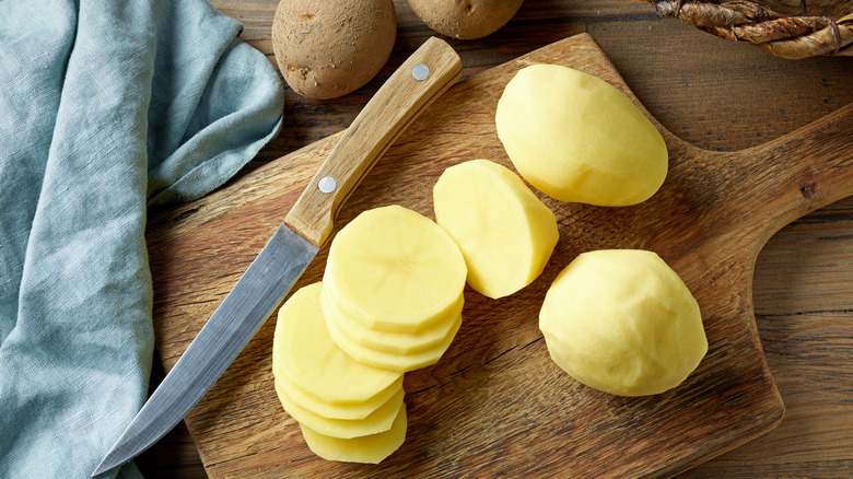 Sliced potatoes on a wooden board with knife