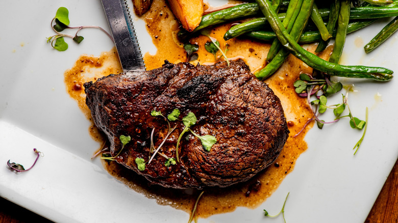 Fancy plate of steak with green beans, potatoes, knife, sauce, and garnish