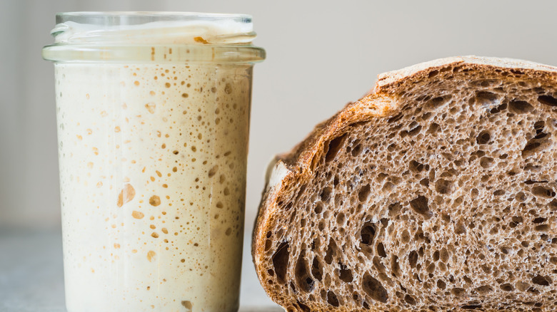 Sourdough starter in a jar next to a loaf of bread