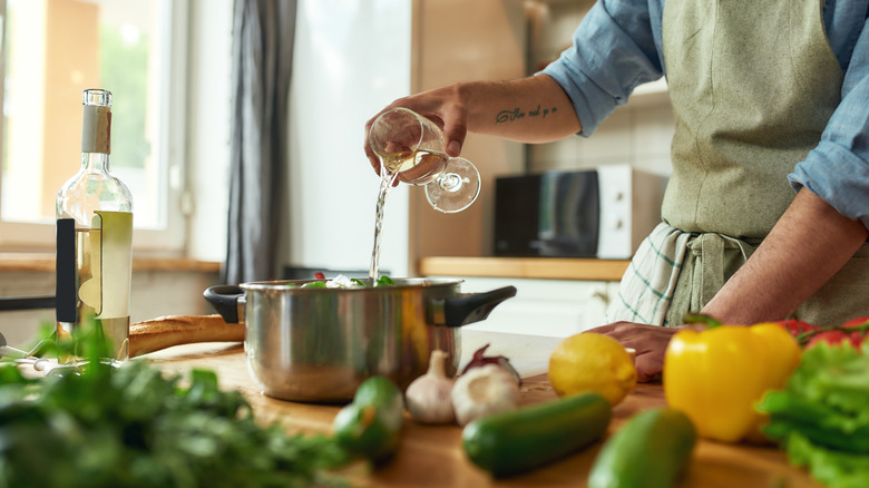 hand pouring wine into pot on cutting board