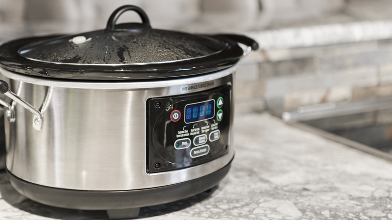 A lidded slow cooker set to low on a marble counter