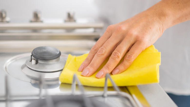 person cleaning stove with yellow sponge