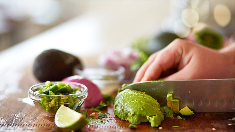 Hands slicing avocado with knife 