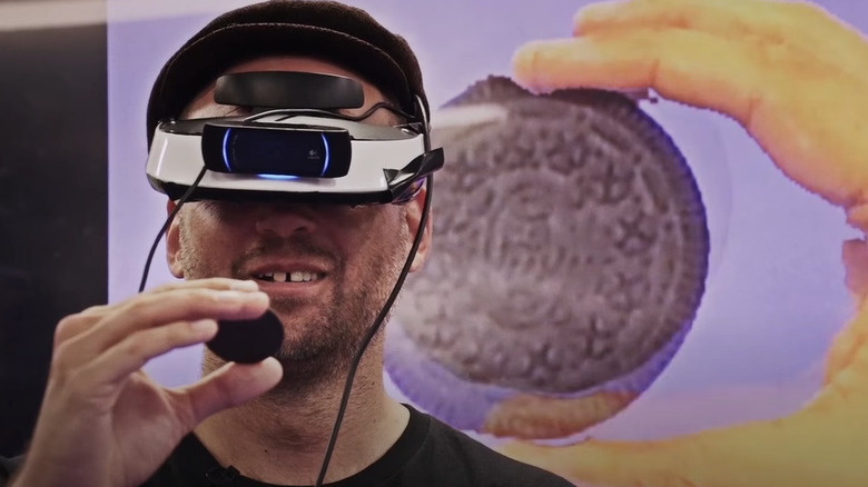 Man virtual reality goggles holding cookie.