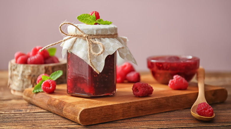 raspberry jam jar on wooden board with fresh raspberries