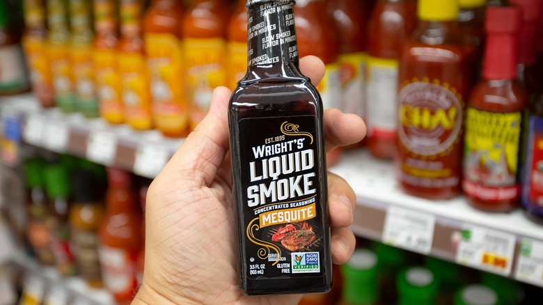 hand holding a bottle of liquid smoke in a grocery store