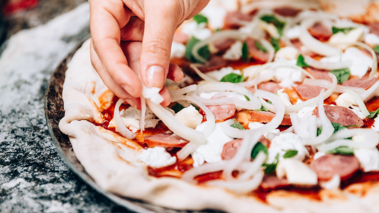 Topping uncooked pizza with salami and onions