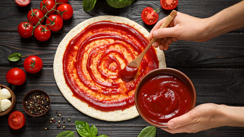 Spreading tomato sauce on pizza with wood spoon