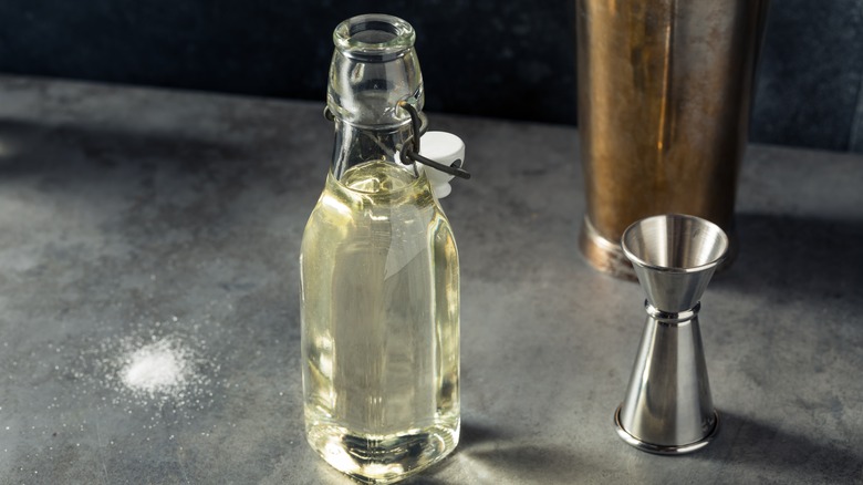 A glass bottle of simple syrup next to a jigger 