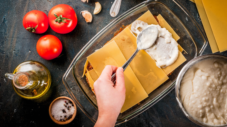 Hands making lasagna in casserole dish