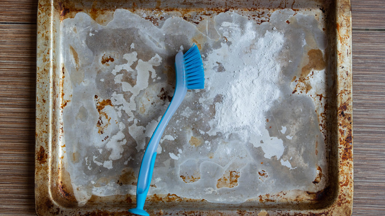 stained baking sheet with white powder and scrubbing brush