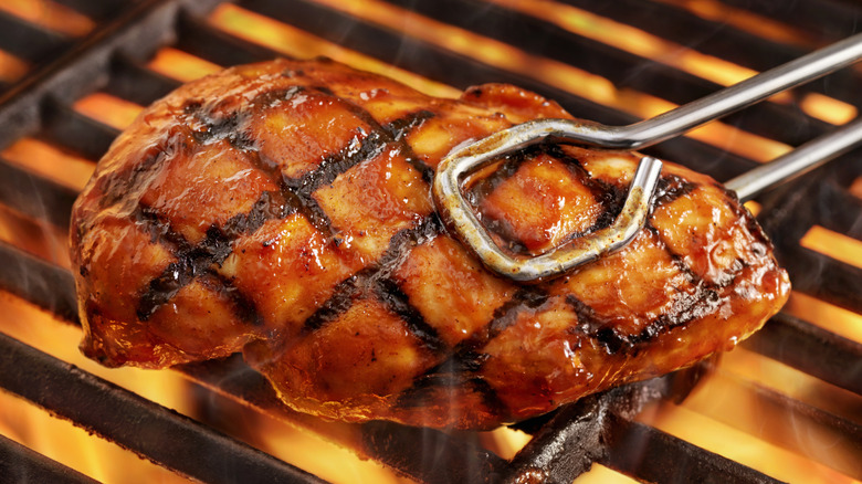 tongs turning chicken on fiery grill