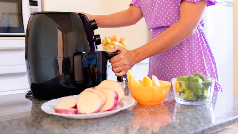 woman next to air fryer and raw cut vegetables 