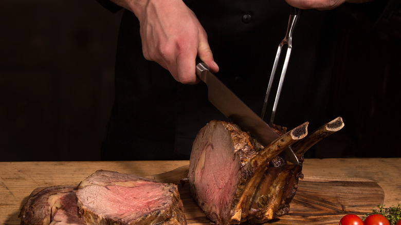 Hands carving a prime rib into slices