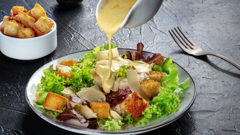 dressing being poured onto a Caesar salad 