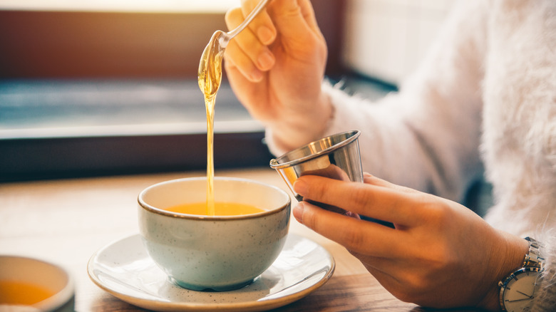 person spooning honey into tea cup