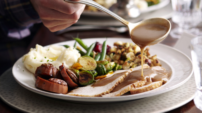 Gravy being ladled over turkey on a plate with sides.