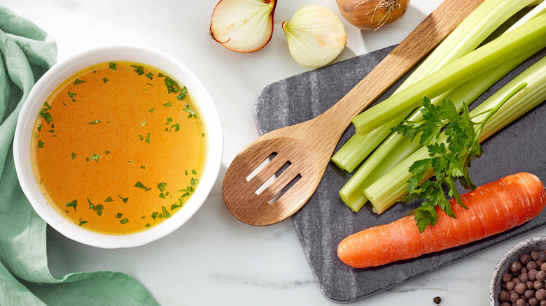 Bowl of chicken bone broth surrounded by its fresh ingredients.