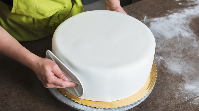 person smoothing out a fondant covering on a cake