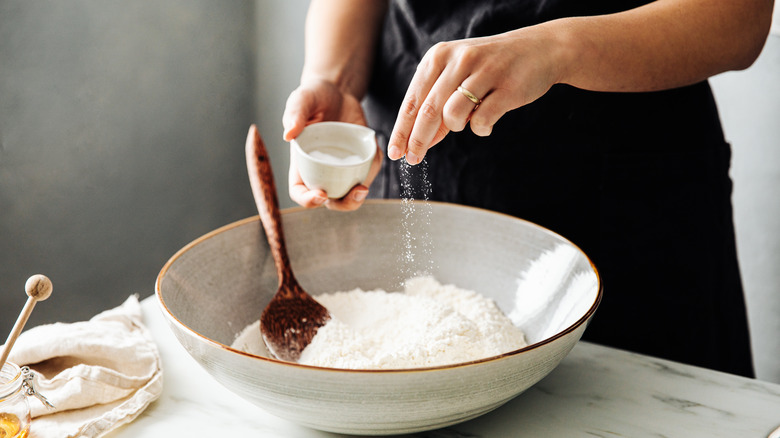 person sprinkling salt into bowl of flour