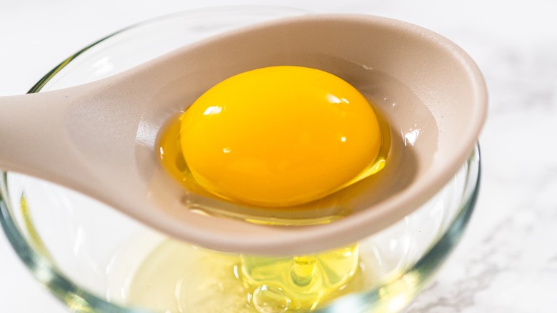 Egg yolk in a slotted spoon over a egg whites in a glass dish