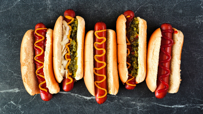 Overhead view of hotdogs with toppings on a dark slate background