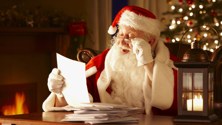 A live-action Santa adjusting his glasses and happily reading a letter