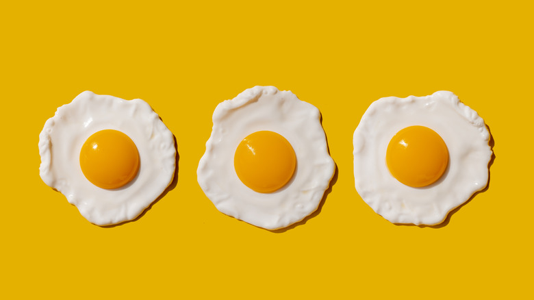 Three plain fried eggs on yellow background