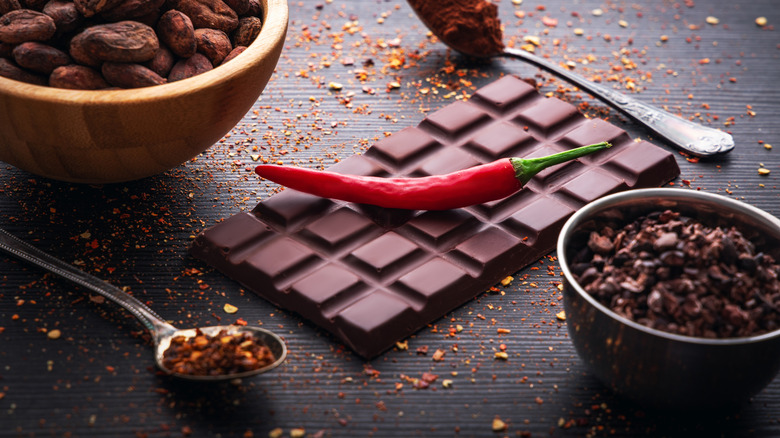 dark chocolate bar with a chili on top and a bowl of cacao beans