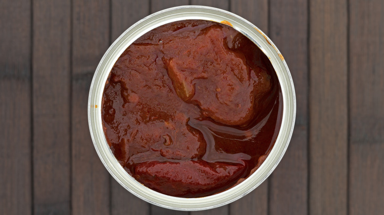 An open can of chipotles in adobo on a wooden table