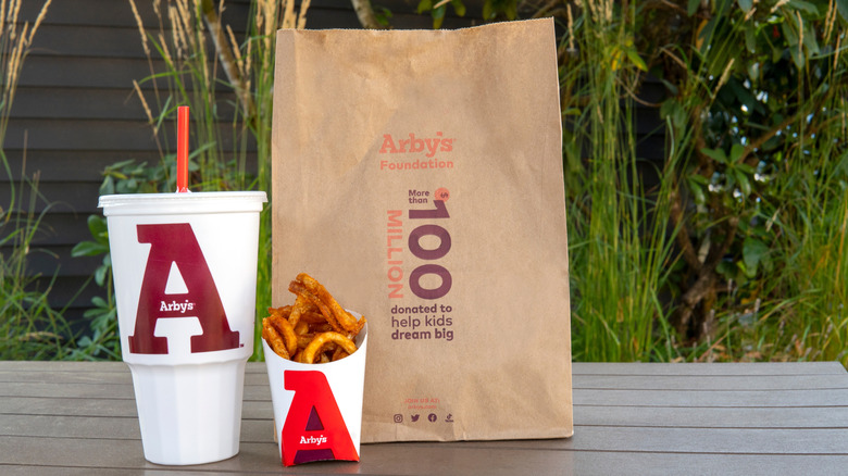 Arby's bag next to a large drink in a plastic cup and a container of curly fries