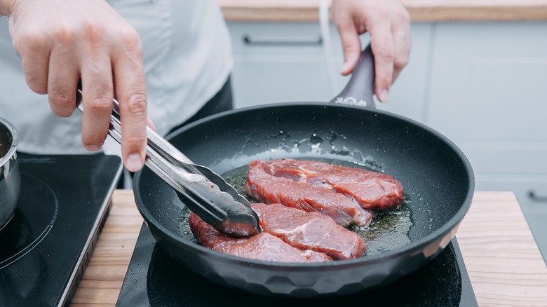 A person cooking steak in a pan