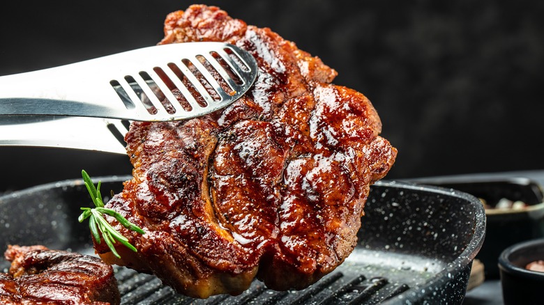 Steak held with tongs over a pan