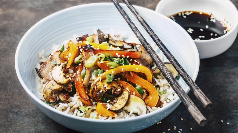 Bowl of stir-fry over rice with chopsticks.