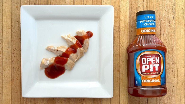 Bottle and white square plateful of chicken with Open Pit Original BBQ Sauce