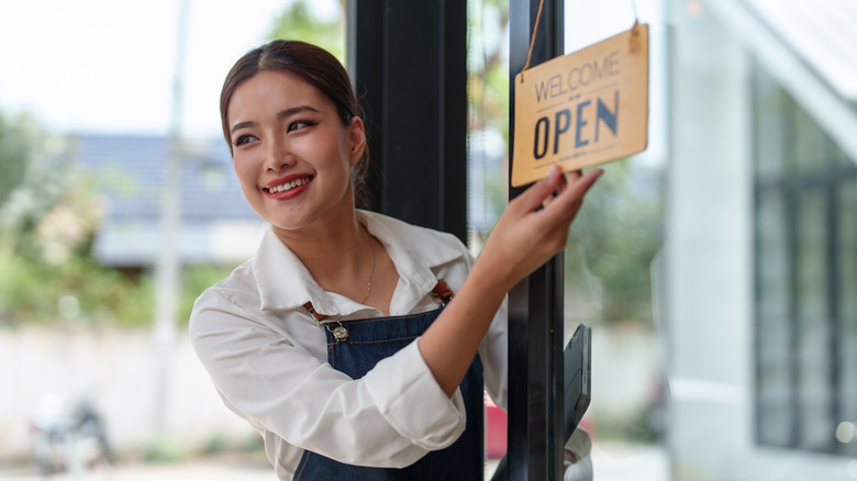 Happy small business owner in apron, holding a hanging "Open" sign